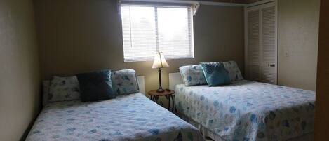 A bedroom with two beds, a window with blinds, a ceiling fan, and a door.