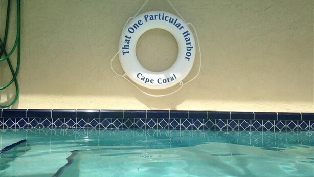 A pool with a lifebuoy labeled "That One Particular Harbor Cape Coral" hanging on the wall. - That One Particular Harbor - Gulf Access Pool Home  3/2 (Cape Coral)