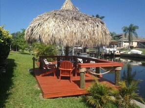 Una terraza de madera con techo de paja, rodeada de agua y vegetación.