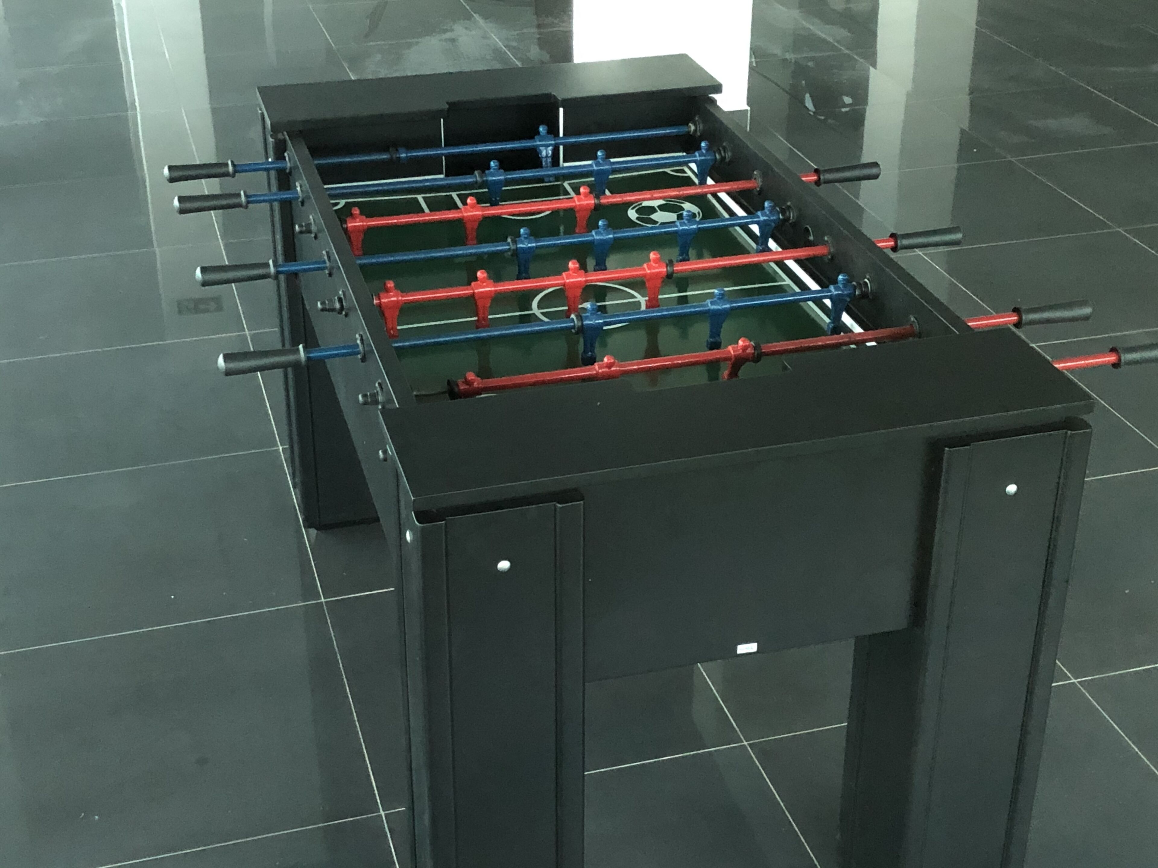 A black foosball table with red and blue players, set on a glossy black floor.