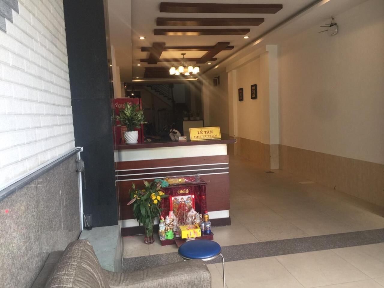 Un área de recepción con un mostrador, un letrero que dice "Lê Tân Reception" y un pequeño altar con ofrendas.