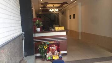 Un área de recepción con un mostrador, un letrero que dice "Lê Tân Reception" y un pequeño altar con ofrendas.