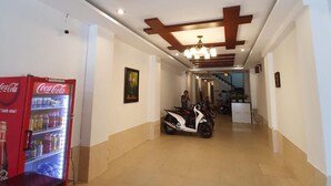 A hallway with a Coca-Cola refrigerator, a scooter, and a ceiling with wooden beams.