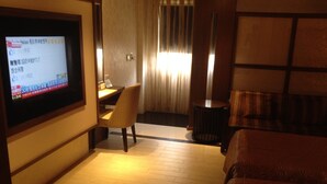 A hotel room with a television on the wall, a desk with a chair, a round table, and a patterned sofa. - Chateau Motel & Spa - Daliao (Kaohsiung)