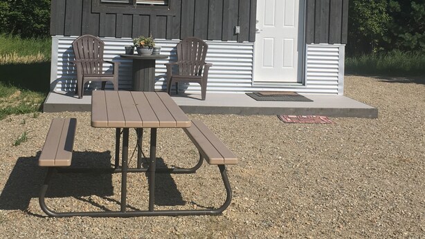 Une petite cabane en bois avec une table de pique-nique et deux chaises devant.