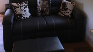 Un canapé en cuir noir agrémenté de coussins à motifs équestres, une corne de bélier fixée au mur et une affiche ancienne accrochée au mur.