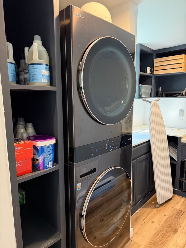 A stacked washer and dryer unit with shelves above containing cleaning supplies.