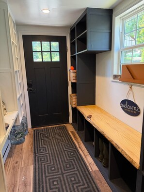 A room with a black door, a welcome sign, a bench, and a window with a view.