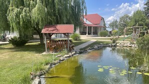 A pond with lily pads, a gazebo, and a house with a red roof.