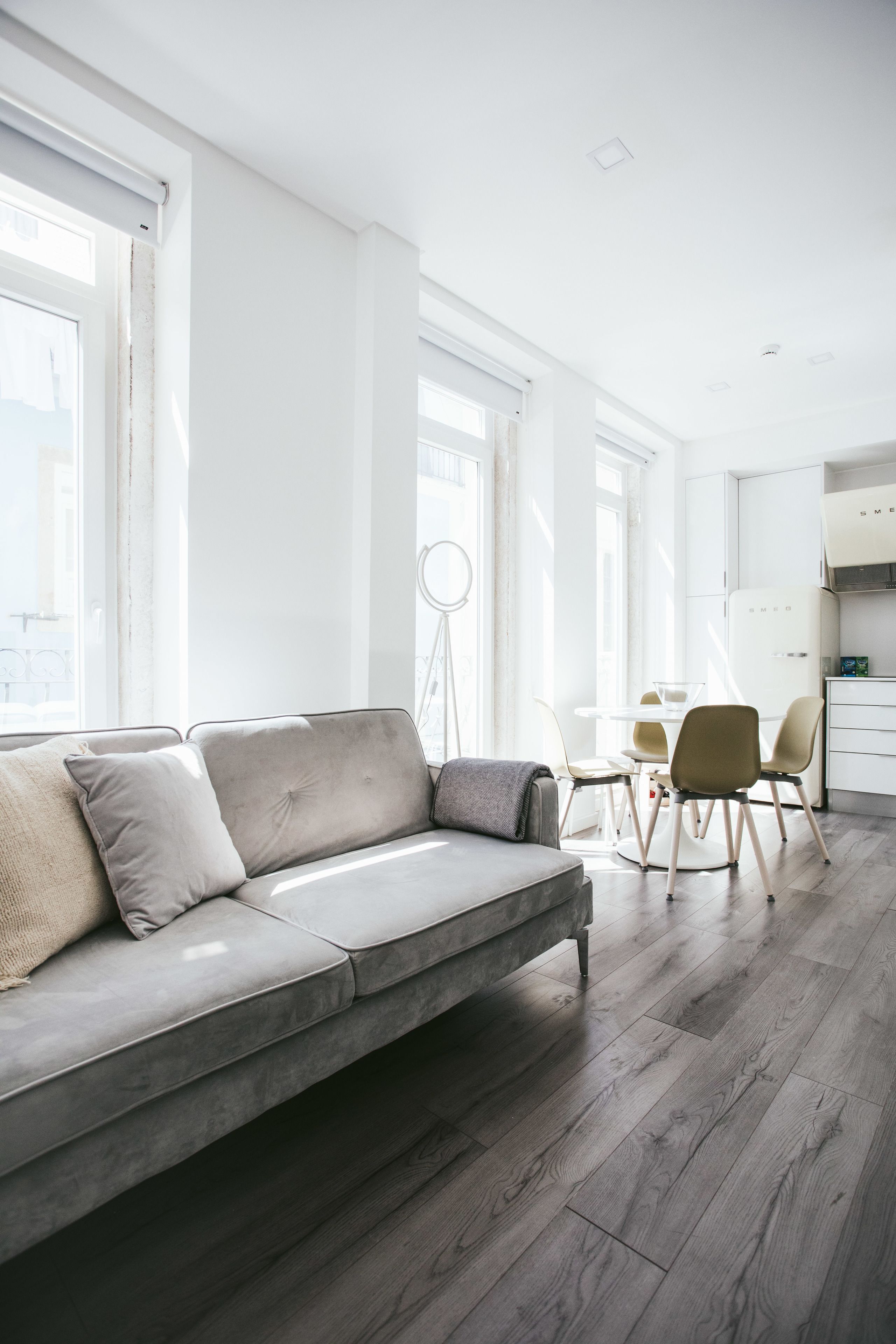 A modern living room with a grey sofa, a dining table with chairs, and a kitchen area in the background.
