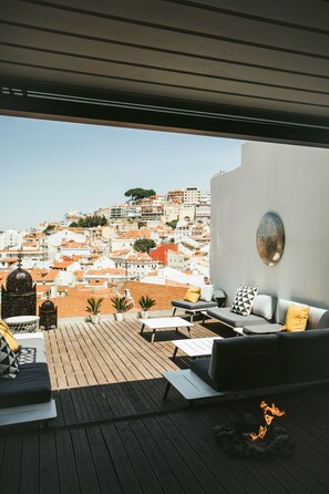 Terrassa al terrat amb vista a un paisatge urbà, moblada amb un sofà, coixins i una petita llar de foc.
