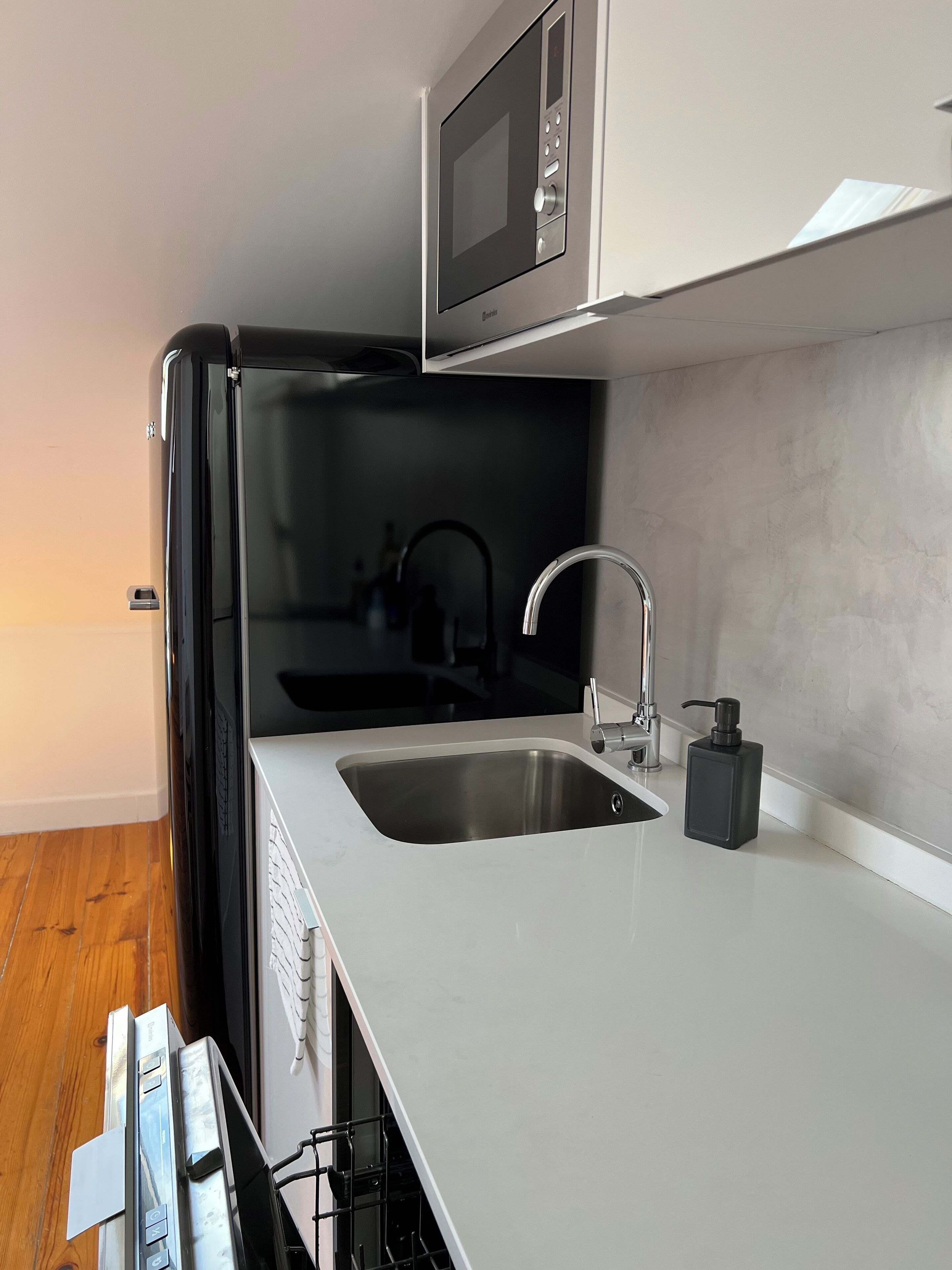 Una cocina compacta con microondas integrado, un lavamanos de acero inoxidable y un grifo negro.