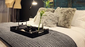 Una cama bien hecha con un almohadón mullido, una mesita de noche con una lámpara y una bandeja con tetera y tazas.