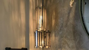 Un tocador de baño con una lámpara moderna, un dispensador de toallas y objetos decorativos, incluyendo un florero con flores y una vela.