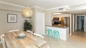 Un espace repas avec une table en bois, des chaises blanches et un luminaire suspendu.