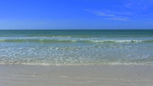 Une plage avec une eau d’un bleu limpide et un rivage sablonneux.