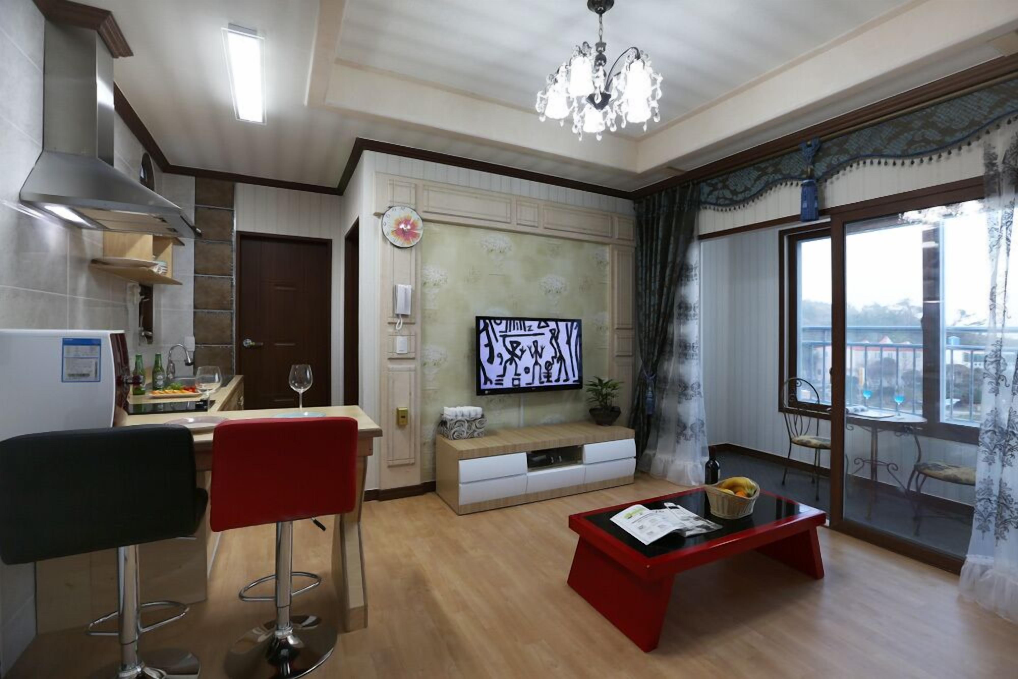 Uma sala de estar moderna com uma mesa de centro vermelha, dois bancos altos, uma televisão e uma janela grande com vista.