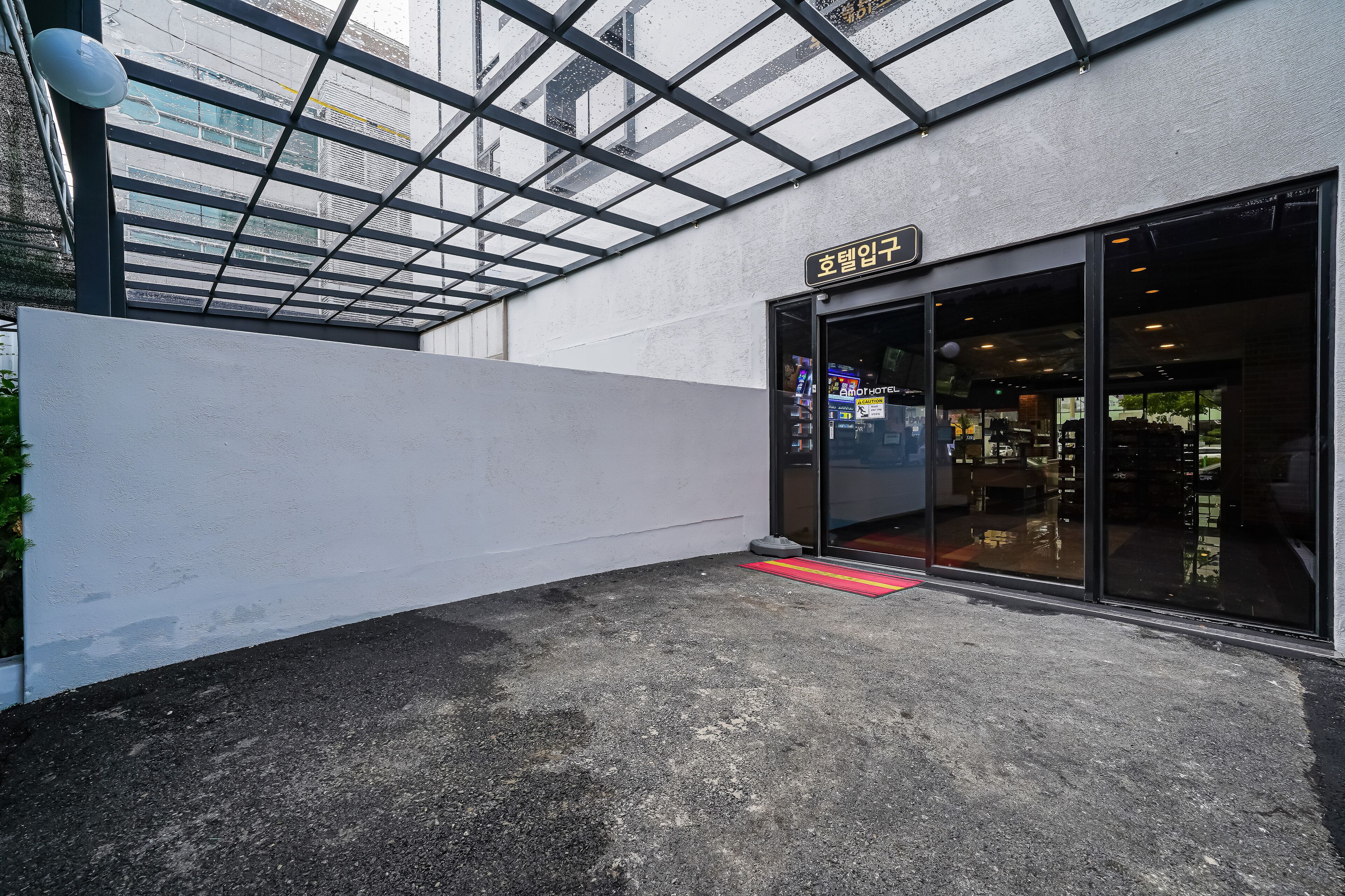 A hotel entrance with a glass door, a red mat, and a sign above the door.