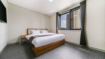 A hotel room with a large bed, a nightstand, a window with curtains, and a view of tall buildings.