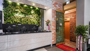 A reception desk with a green leafy wall and a neon sign, a red carpet, and a potted plant. - Masan Amor Hotel (Changwon)