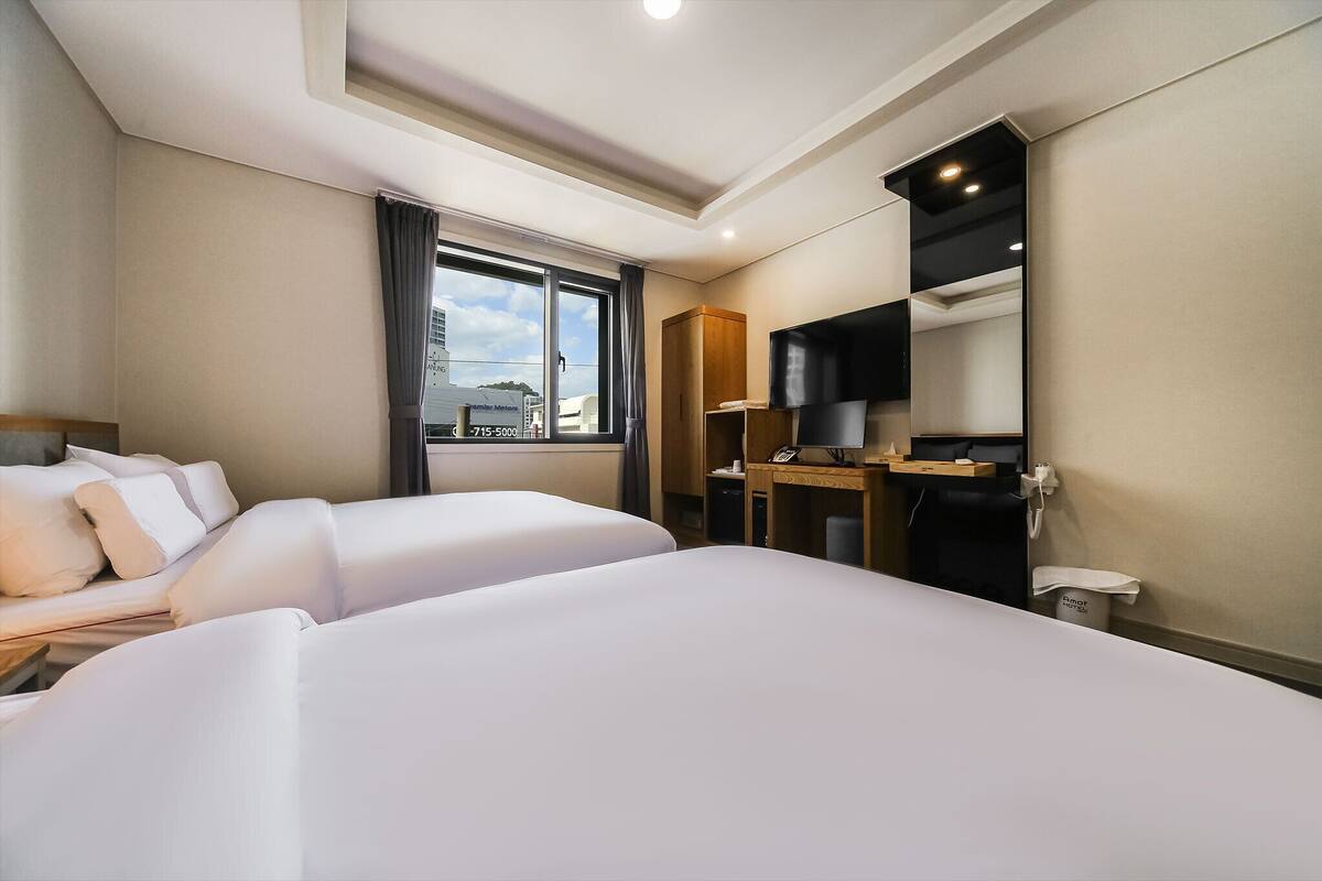 A hotel room with two beds, a desk, a TV, and a window with curtains.