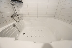 Eine weiße Badewanne mit Duschkopf, Bedienfeld, gefliesten Wänden und Abfluss.