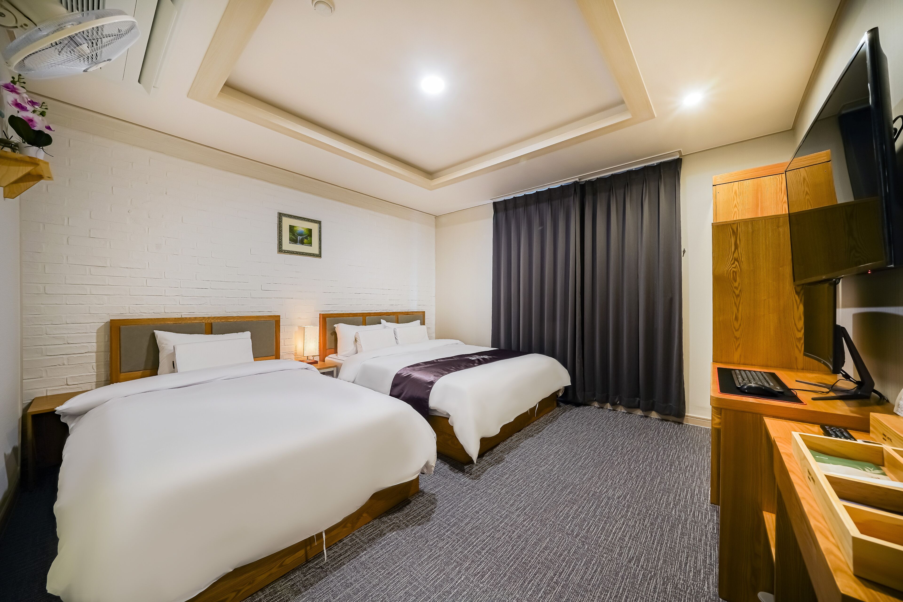 Habitación de hotel con dos camas, un escritorio con computadora, un televisor y un ventilador de techo.