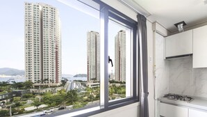 A modern kitchen with a gas stove, white cabinets, and a view of tall buildings and greenery outside. - Masan Amor Hotel (Changwon)
