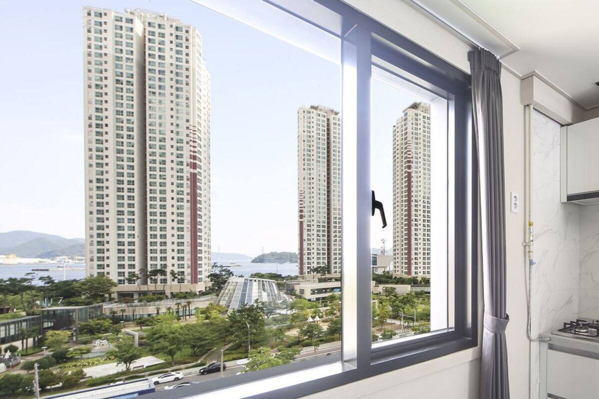 A modern kitchen with a gas stove, white cabinets, and a view of tall buildings and greenery outside.