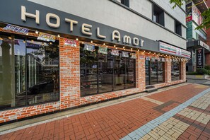 Ein Hotel namens "HOTEL AMOR" mit großen Fenstern und Hinweisschildern "GEÖFFNET".