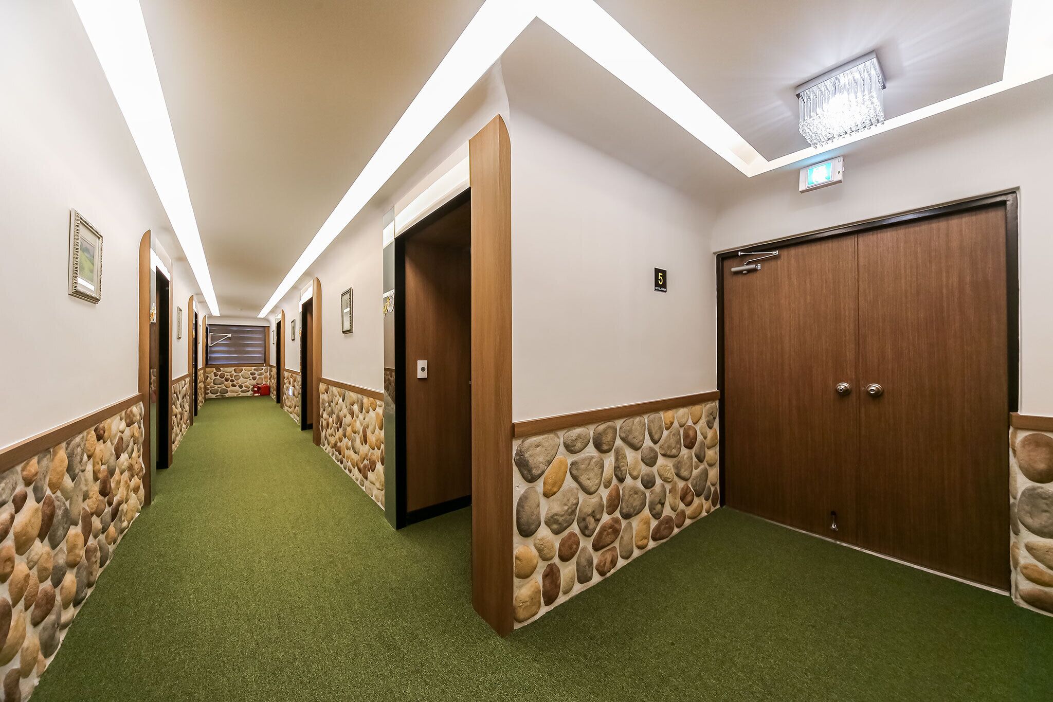 A hotel hallway with a stone accent wall, green carpet, and wooden doors.
