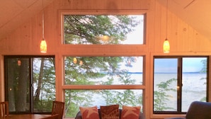 A cozy room with a large window overlooking a body of water, a plaid sofa with cushions, and two wooden chairs. - Intimate cottage near Acadia national park (Mariaville)