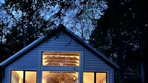 A two-story cabin with large windows, a covered front porch, and a stone pathway leading to the entrance. - Intimate cottage near Acadia national park (Mariaville)