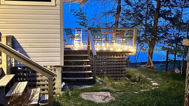 A wooden deck with a staircase leading to a covered area, surrounded by trees and a grassy path. - Intimate cottage near Acadia national park (Mariaville)