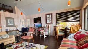 A cozy living room with a wooden ceiling, a television, a sofa, and a dining area with chairs and a table. - Intimate cottage near Acadia national park (Mariaville)