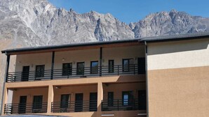 Un edificio de dos pisos con balcones, con montañas al fondo.