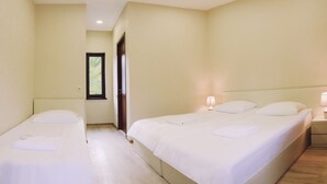 Habitación de hotel con dos camas individuales, una mesita de noche con lámpara y una puerta que da a otra habitación.