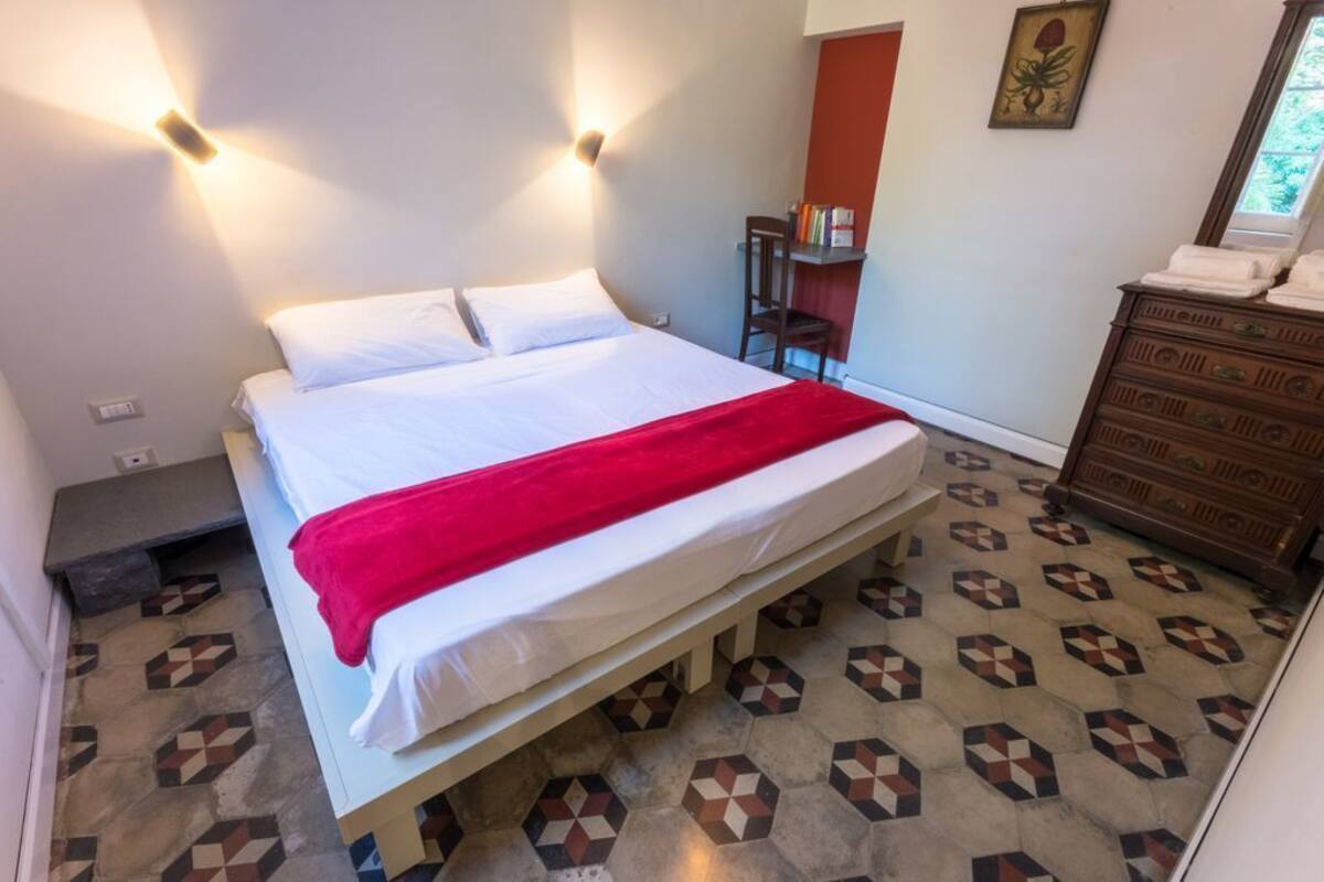 A bed with a red blanket, a wooden dresser, and a patterned floor.