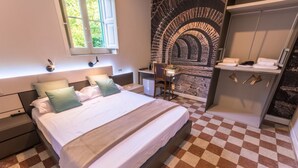 Een slaapkamer met een geruite vloer, een bed met kussens, een bureau met stoel, een stenen muur en een kledingkast.