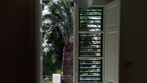 Een open doorgang naar een balkon met uitzicht op groen en een palmboom.