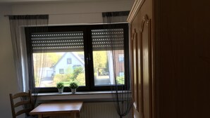 Ein Zimmer mit Holztisch und Stuhl, einem Fenster mit Jalousien und Blick auf ein Haus.