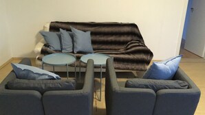 Ein Wohnzimmer mit einem dunkelbraunen Sofa, zwei grauen Sesseln und zwei kleinen runden Tischen.