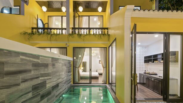 Ein modernes Interieur mit einem gläsernen Pool, einem mit Pflanzen bepflanzten Balkon und einem sichtbaren Schlafzimmer mit Bett und Vorhängen.