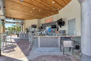 An outdoor kitchen area with a bar, seating, and a TV mounted on the wall.