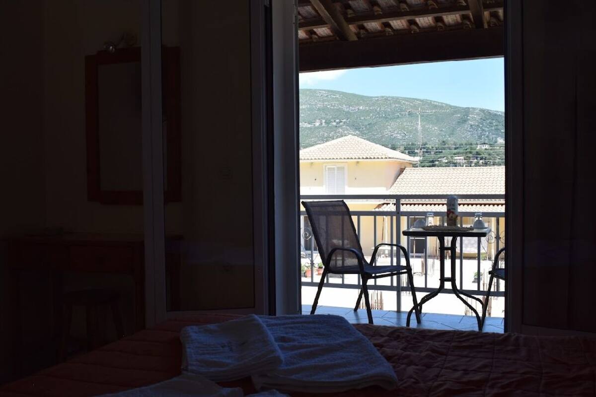 A bedroom with a bed, a window, and a view of a balcony with chairs and a table.