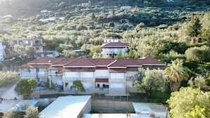 A residential building with multiple balconies, a swimming pool, and a view of a hilly landscape. - Villa Miranda (Zakynthos)