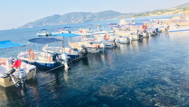 A marina with various boats docked, clear water, and a hilly landscape in the background. - Villa Miranda (Zakynthos)