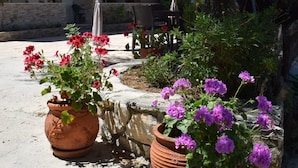 A patio area with potted plants, a bench, and a building with a balcony. - Villa Miranda (Zakynthos)