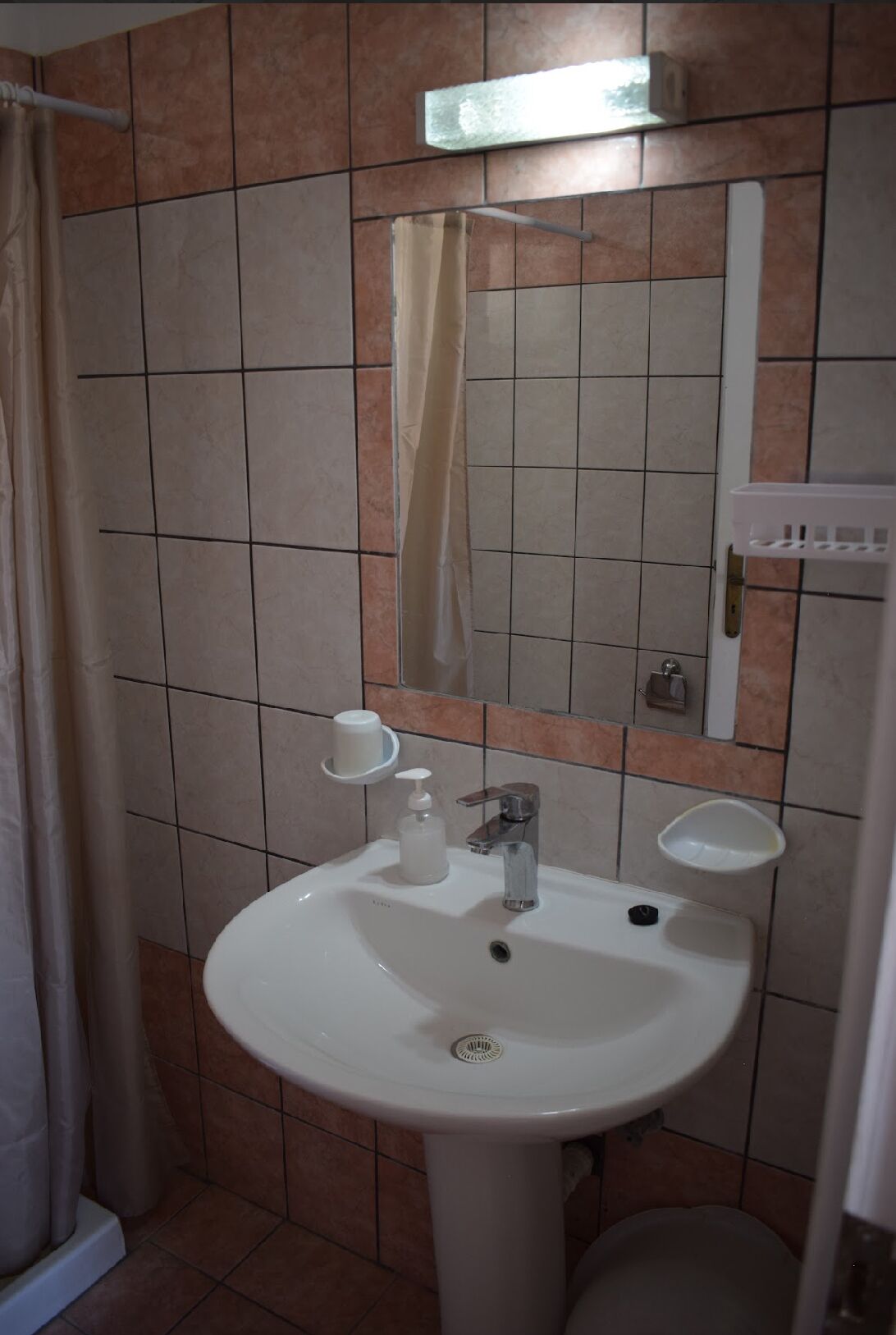 A bathroom with a white sink, a mirror, a shower curtain, and a small shelf with toiletries.