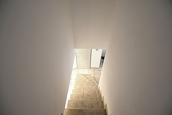 A narrow stairway leading to a room with a white door and a tiled floor. - Mhost Bronowice (Kraków)